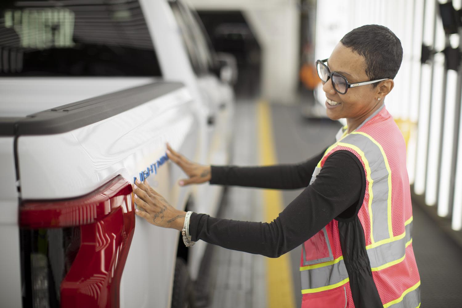 A Ford plant worker places a vehicle badge on an F-150 Lightning