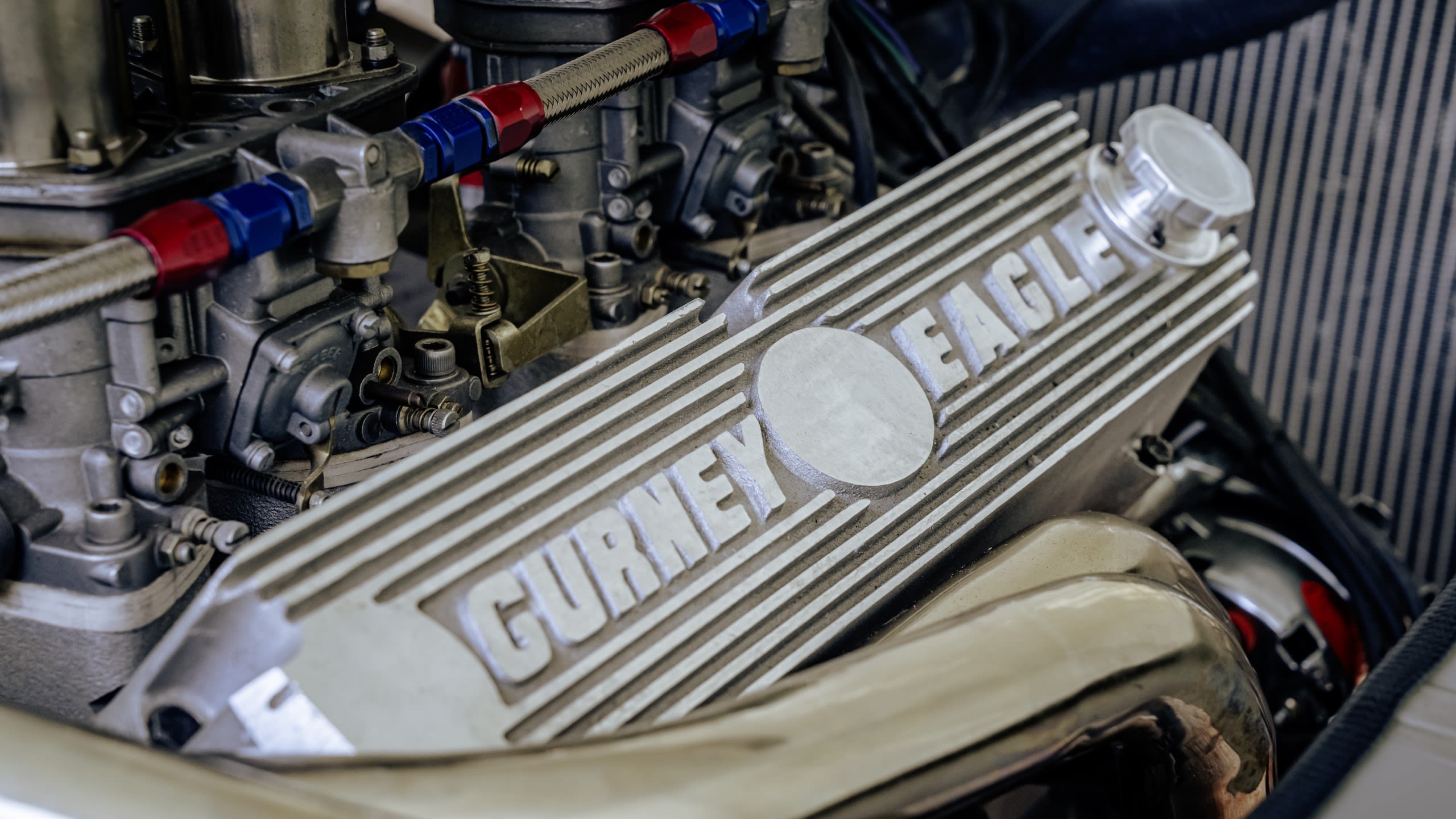 Gurney Eagle logos on engine cover of the Ford V8 in Supervan 1. Exhaust, headers and intakes around the edge of the close-up shot.